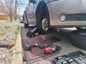 Car on a jack with a mechanic’s tools, including a Milwaukee impact wrench, on a mat beside a Denver street, showcasing auto repair in Denver services by AutoFordable Mobile Mechanics.