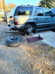 Mobile mechanic near me in Denver repairing a vehicle with a removed tire, jack, and tools in a driveway