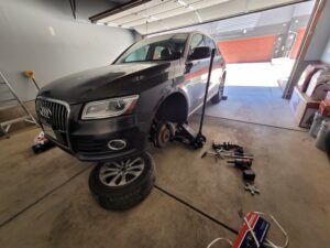 Mobile mechanic near me in Denver working on a vehicle in a garage, with the front end jacked up, tire removed, and tools scattered