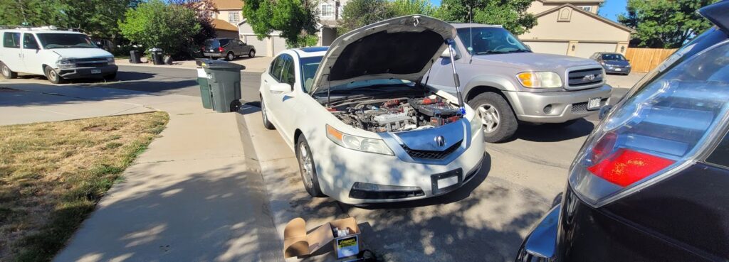 Mobile mechanic in Denver repairing a white Acura on a residential street