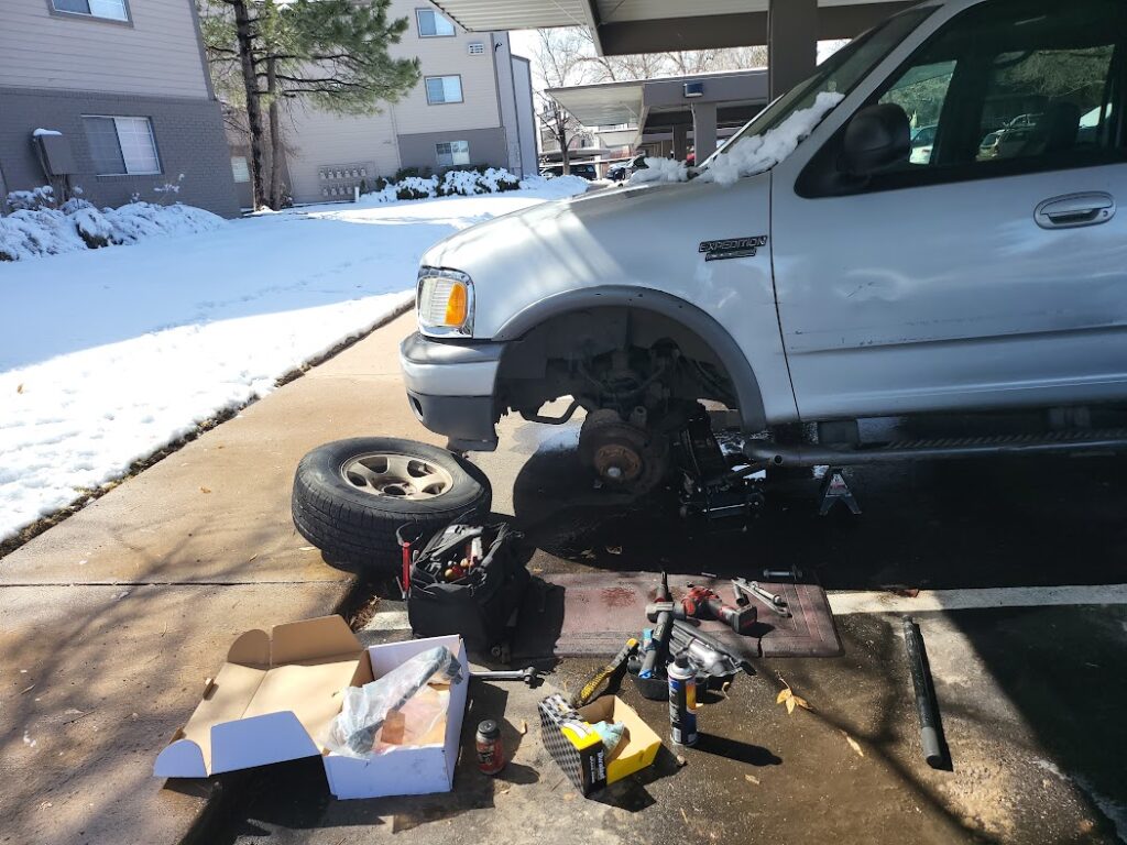 Denver mobile mechanic repairing a Ford Expedition at a customer’s home in snowy conditions with tools and parts.