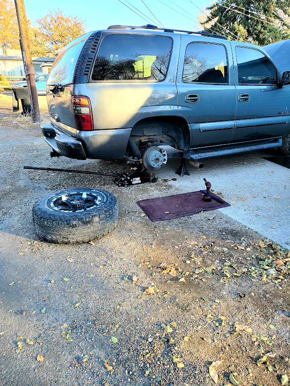 Mobile mechanic in Fort Worth performing a brake repair on a silver SUV near the customer’s driveway with a jack and tools.