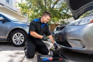 Mobile mechanic near me inspecting and replacing a car battery in a driveway, offering fast auto repair services in Denver.