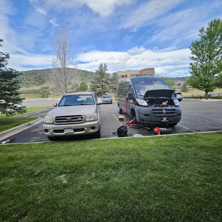 AutoFordable mobile mechanic performing alternator repair on a van in a Denver parking lot with a Toyota SUV nearby, showcasing on-site car repair services.