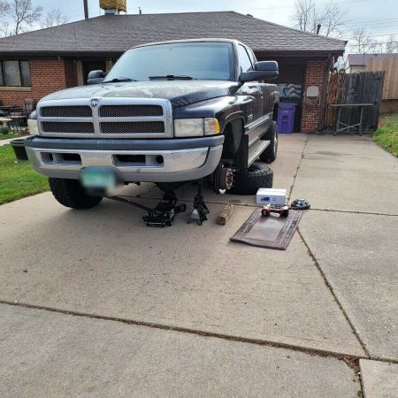 Raised front view of a black pickup truck elevated on jack stands in a residential driveway, with tools and equipment for mobile auto repair services visible, emphasizing convenient on-site mechanic services.