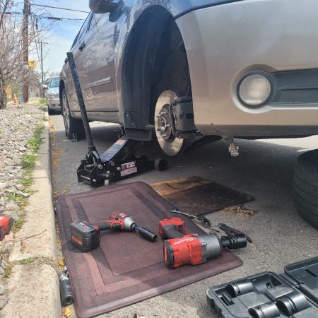 Car on a jack with a mechanic’s tools, including a Milwaukee impact wrench, on a mat beside a Denver street, showcasing auto repair in Denver services by AutoFordable Mobile Mechanics.