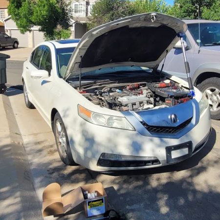 Mobile mechanic in Denver repairing a white Acura on a residential street