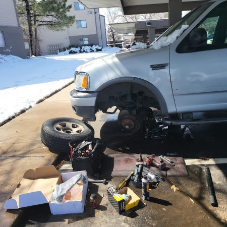 Denver mobile mechanic repairing a Ford Expedition at a customer’s home in snowy conditions with tools and parts.