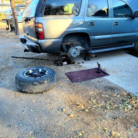 Mobile mechanic in Fort Worth performing a brake repair on a silver SUV near the customer’s driveway with a jack and tools.
