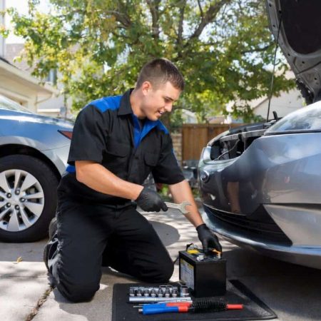 Mobile mechanic near me inspecting and replacing a car battery in a driveway, offering fast auto repair services in Denver.